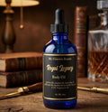 Blue bottle of 'My Unicorn Beauty Royal Legacy Body Oil' on a wooden surface with books and a decanter in the background.