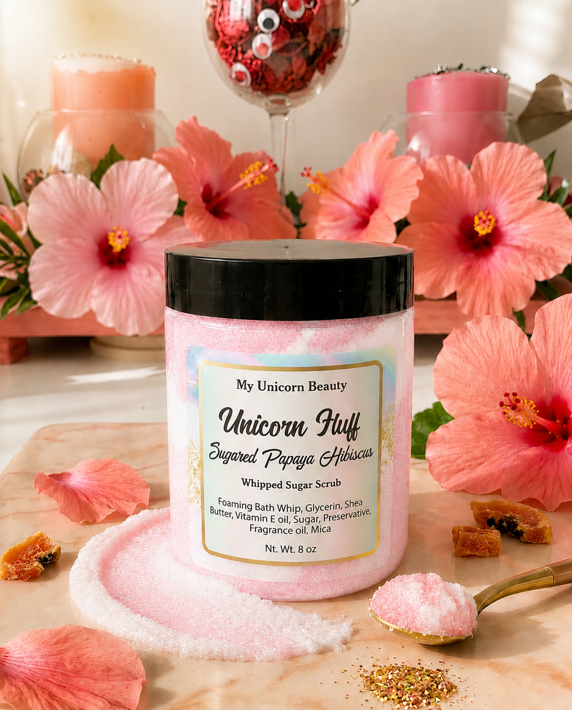 Pink whipped sugar scrub with black lid labeled 'My Unicorn Beauty Unicorn Fluff' on a wooden surface with pink flowers and a glass of red wine in the background.