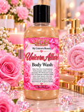 A bottle of My Unicorn Beauty Unicorn Allure Body Wash, filled with a light golden-amber liquid, set against a highly stylized pink and gold background featuring roses, crystals, and a pink towel.